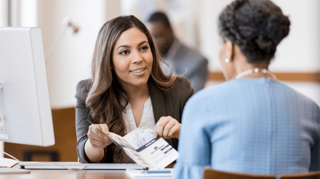 A woman handing documents to a client across a desk in an office.