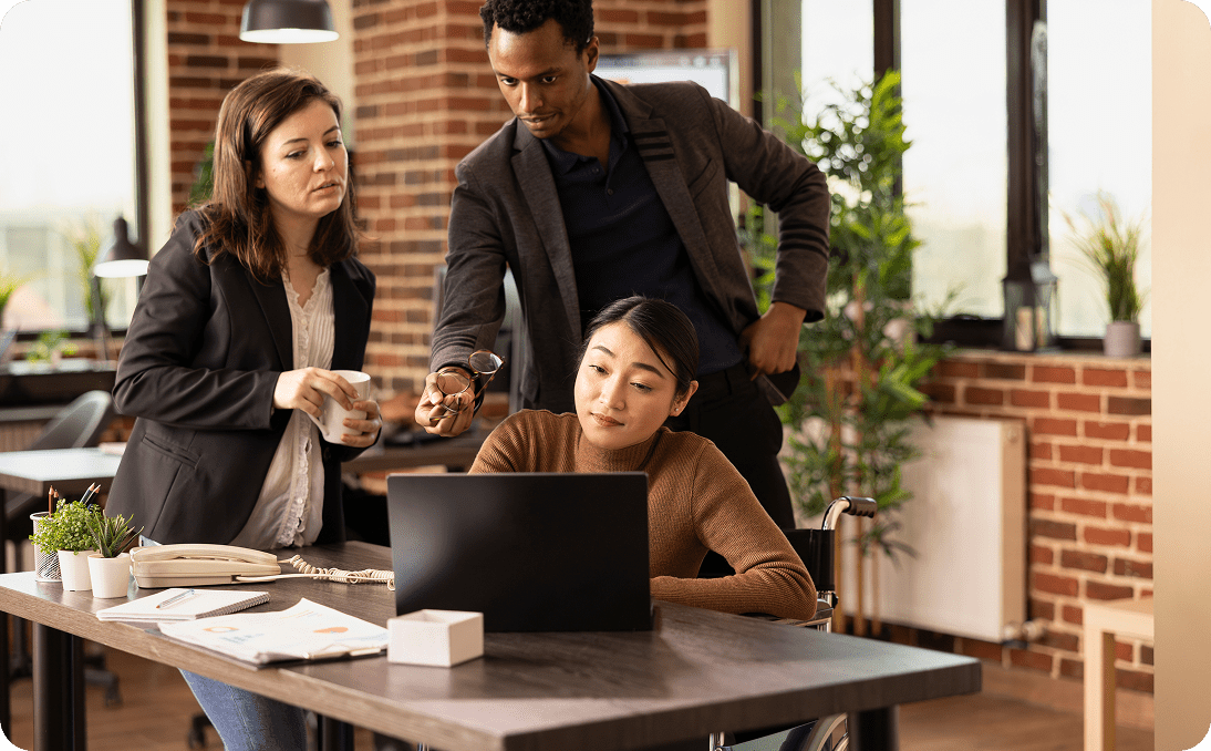 Three coworkers collaborating around a laptop in a modern office