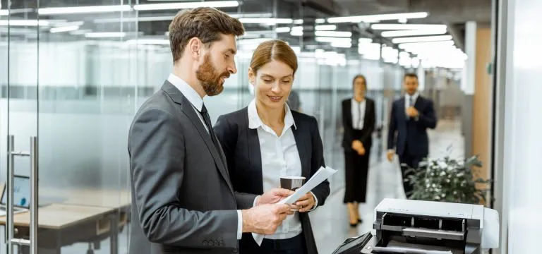 Two people reviewing documents together in a modern office hallway.