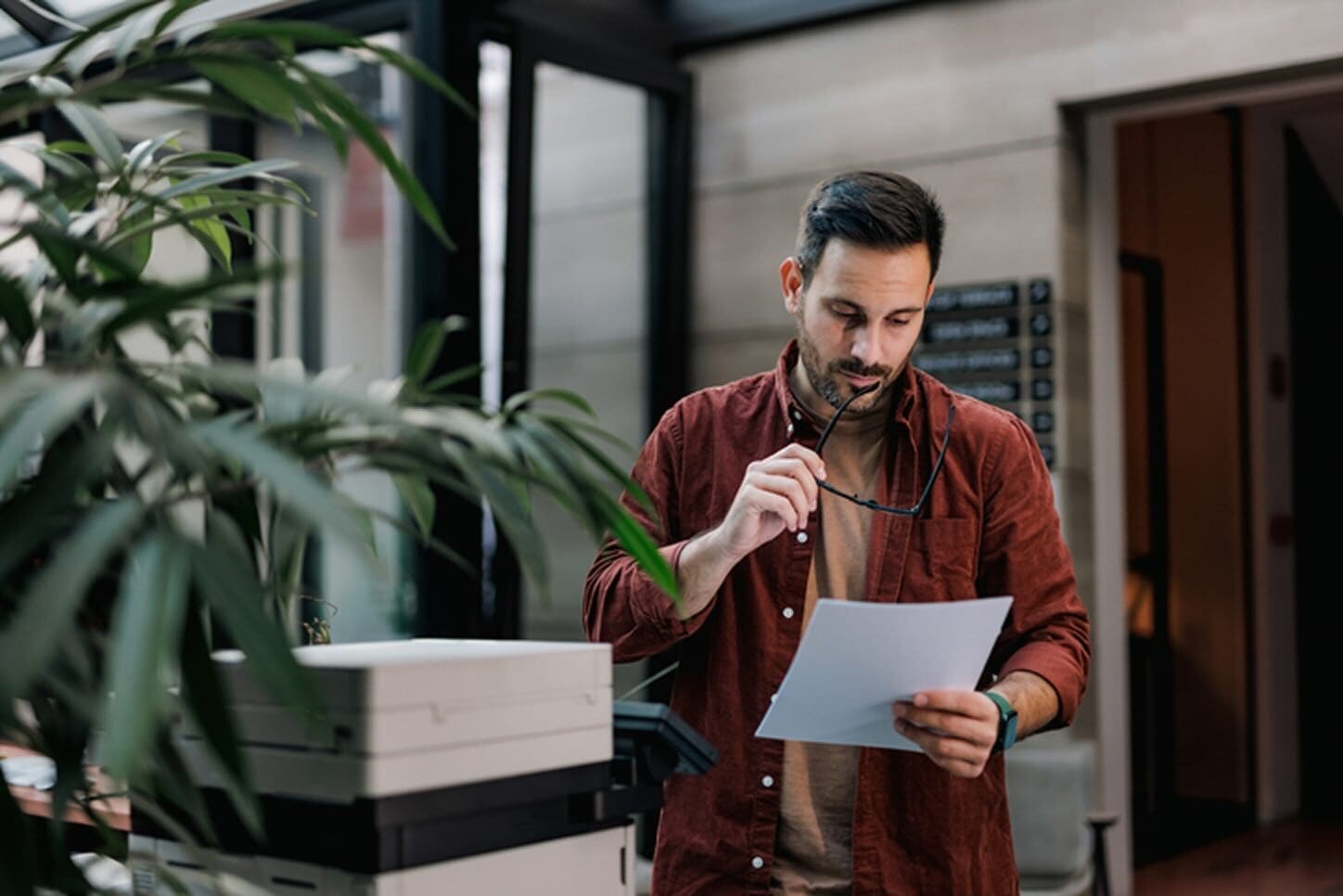 Employee reviewing a printed document beside an office printer, illustrating Print as a Service and cloud-based print management in a modern workplace.