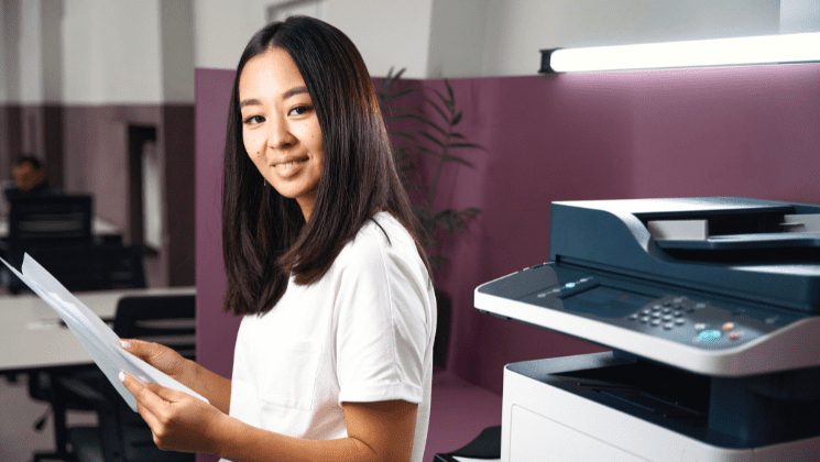 Woman holding printed documents beside an office printer