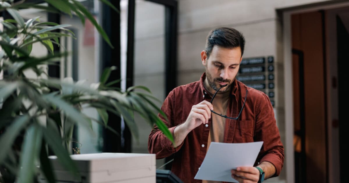 Man in front of a plant, holding a paper while looking at it.