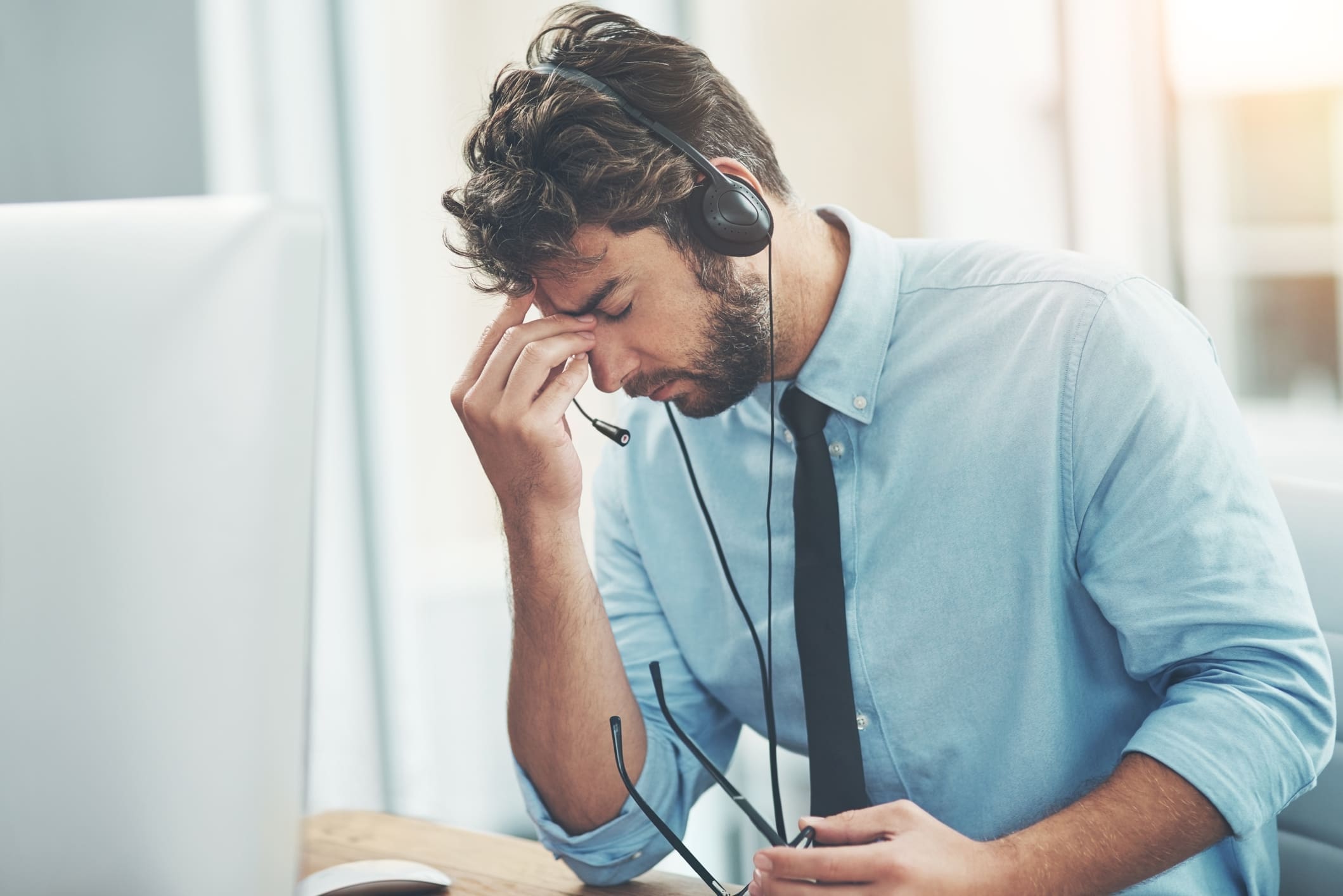 A man holding his forehead while looking stressed in an office.