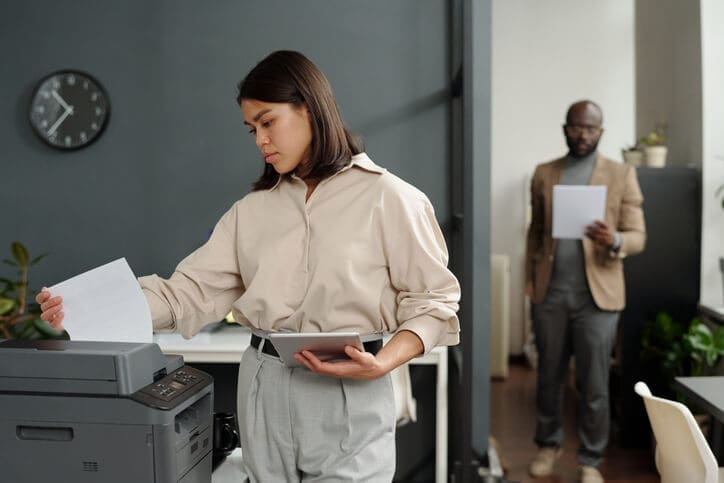 Employee using a printer and tablet, representing print analytics, secure release, and standardized print workflows.